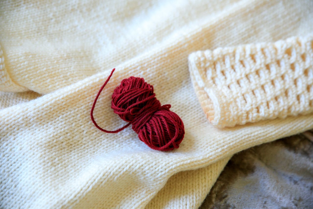 Red yarn ball on a cream woolen blanket, ideal for knitting and making cozy crafts.