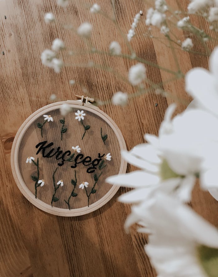 Floral embroidery in hoop with daisies on wooden surface with blurred foreground flowers