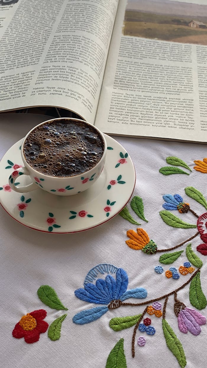 A cup of black coffee on an embroidered tablecloth with a magazine, perfect for a relaxing morning.