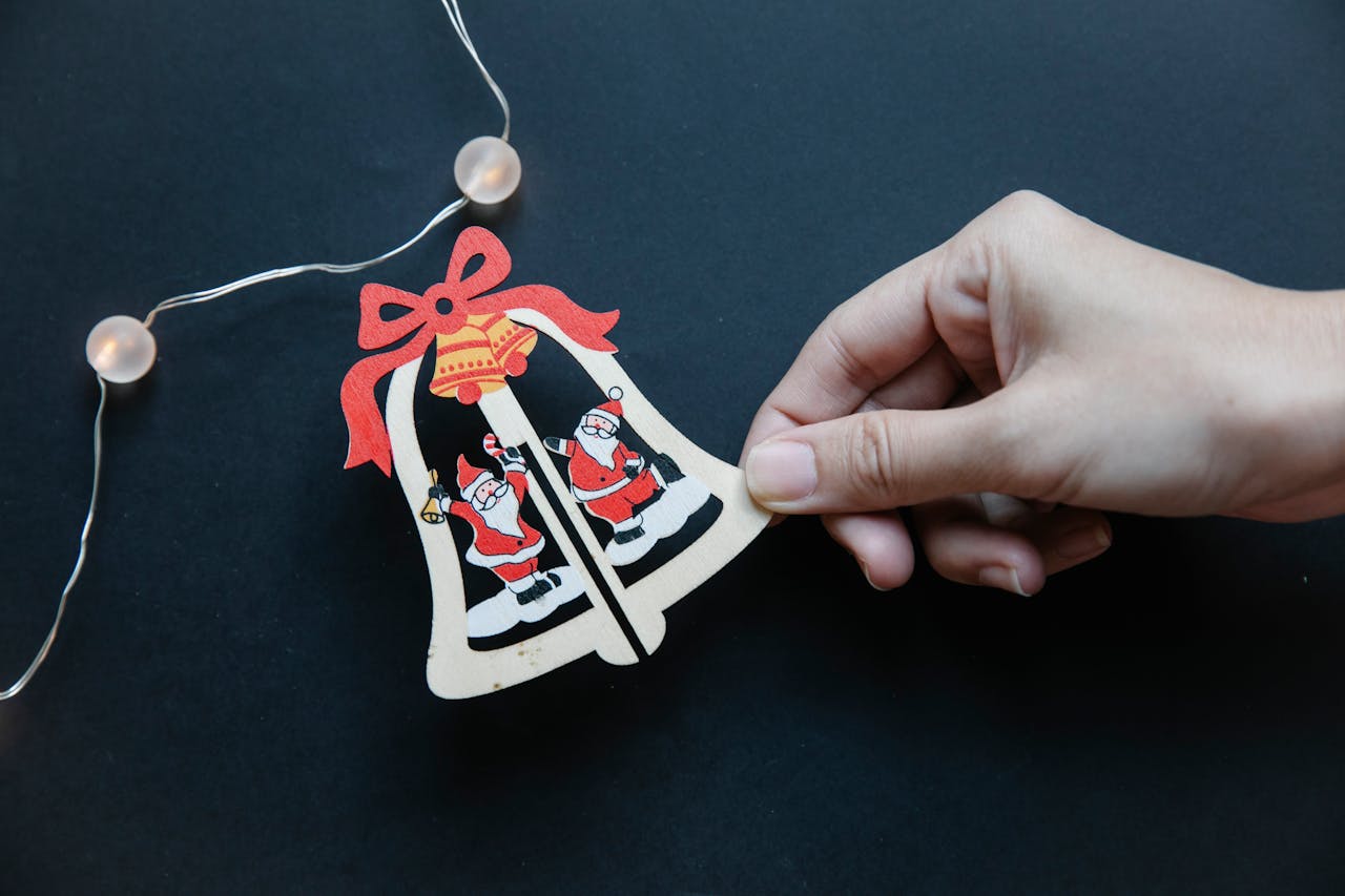 Hand holding a Santa Claus ornament on a black background with decorative lights.